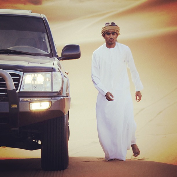 a man in white standing next to his truck in the desert