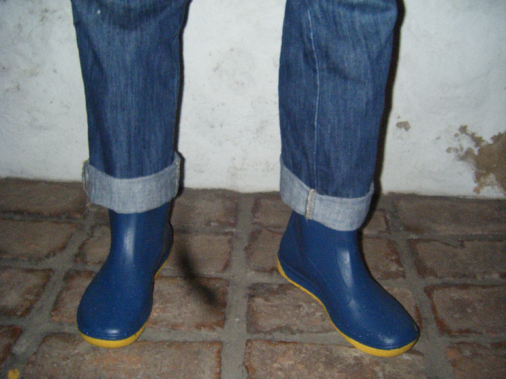 the feet are wearing blue rubber boots and jeans