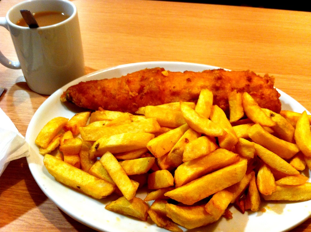 fried fish and fries sit next to a mug
