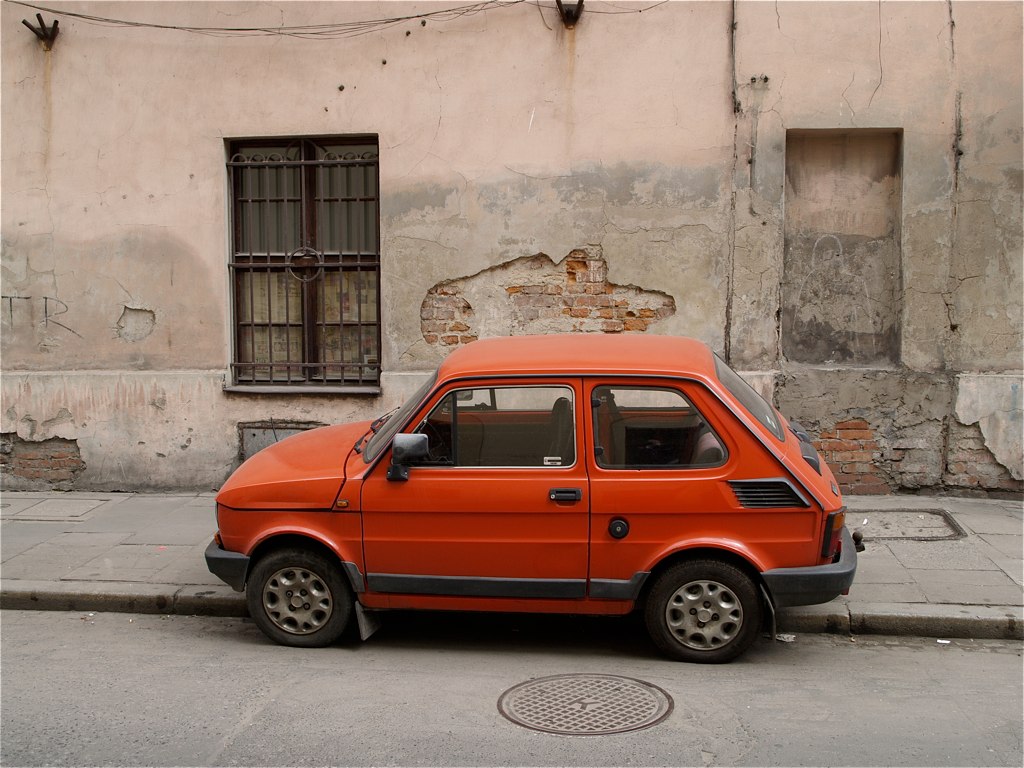 an old red car sitting in the middle of a sidewalk