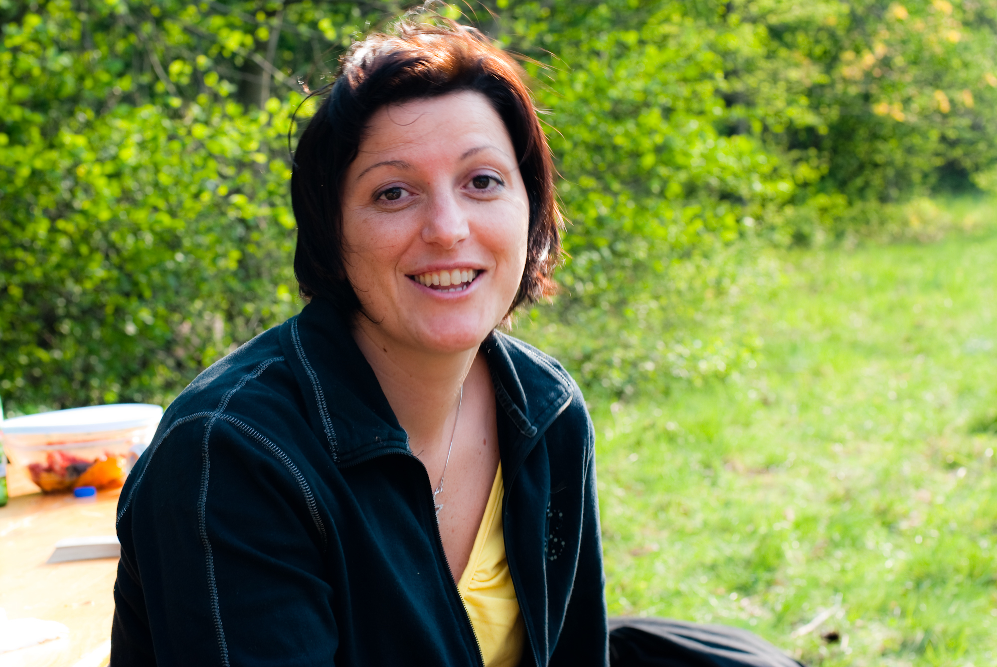 a woman sitting at a table outside smiling