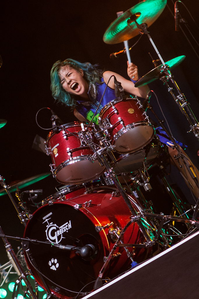 a woman with green hair is playing the drums