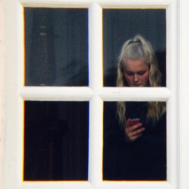 a woman looking out a window holding a phone