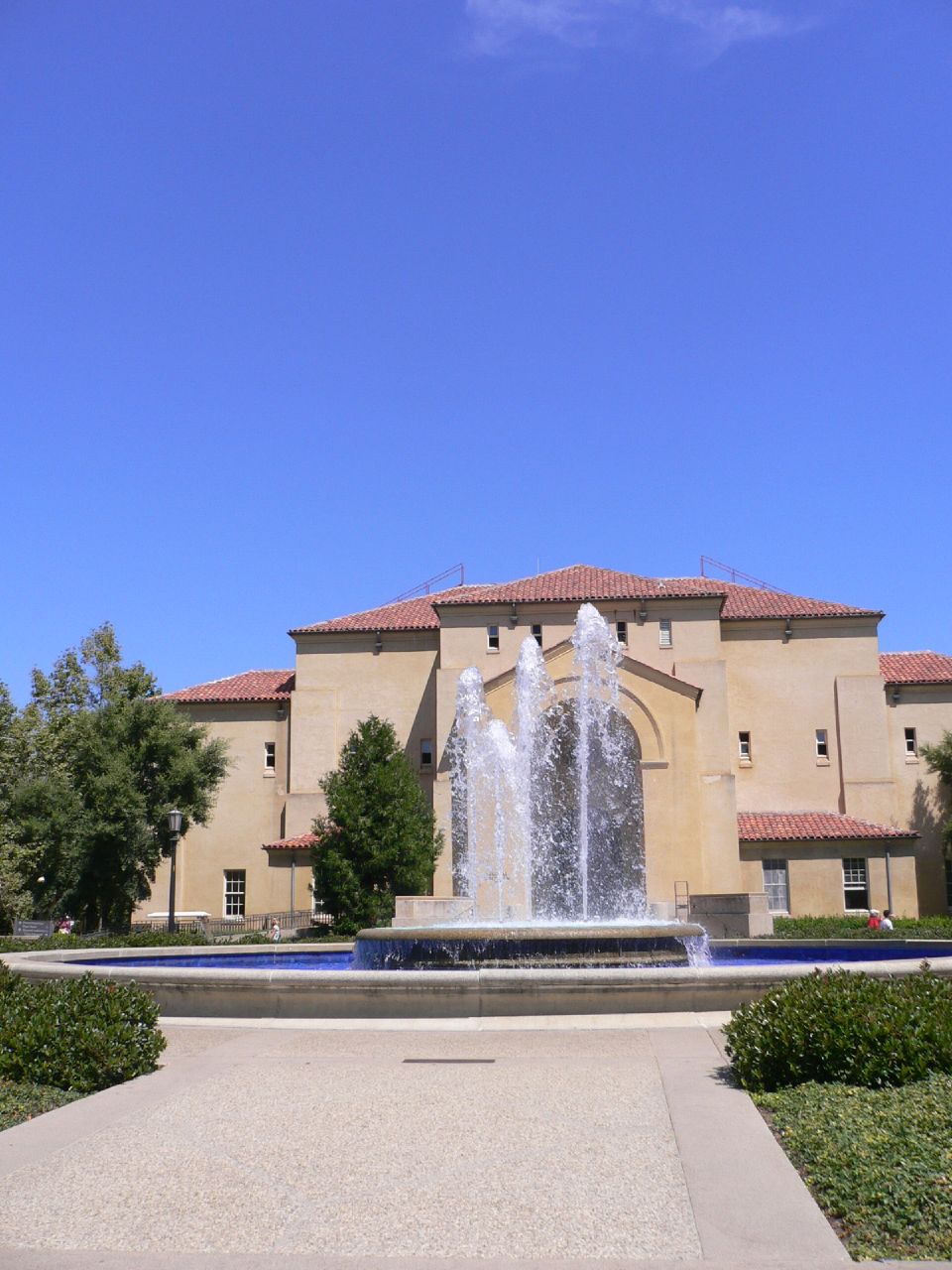a fountain with many water features and plants in front of an orange colored building