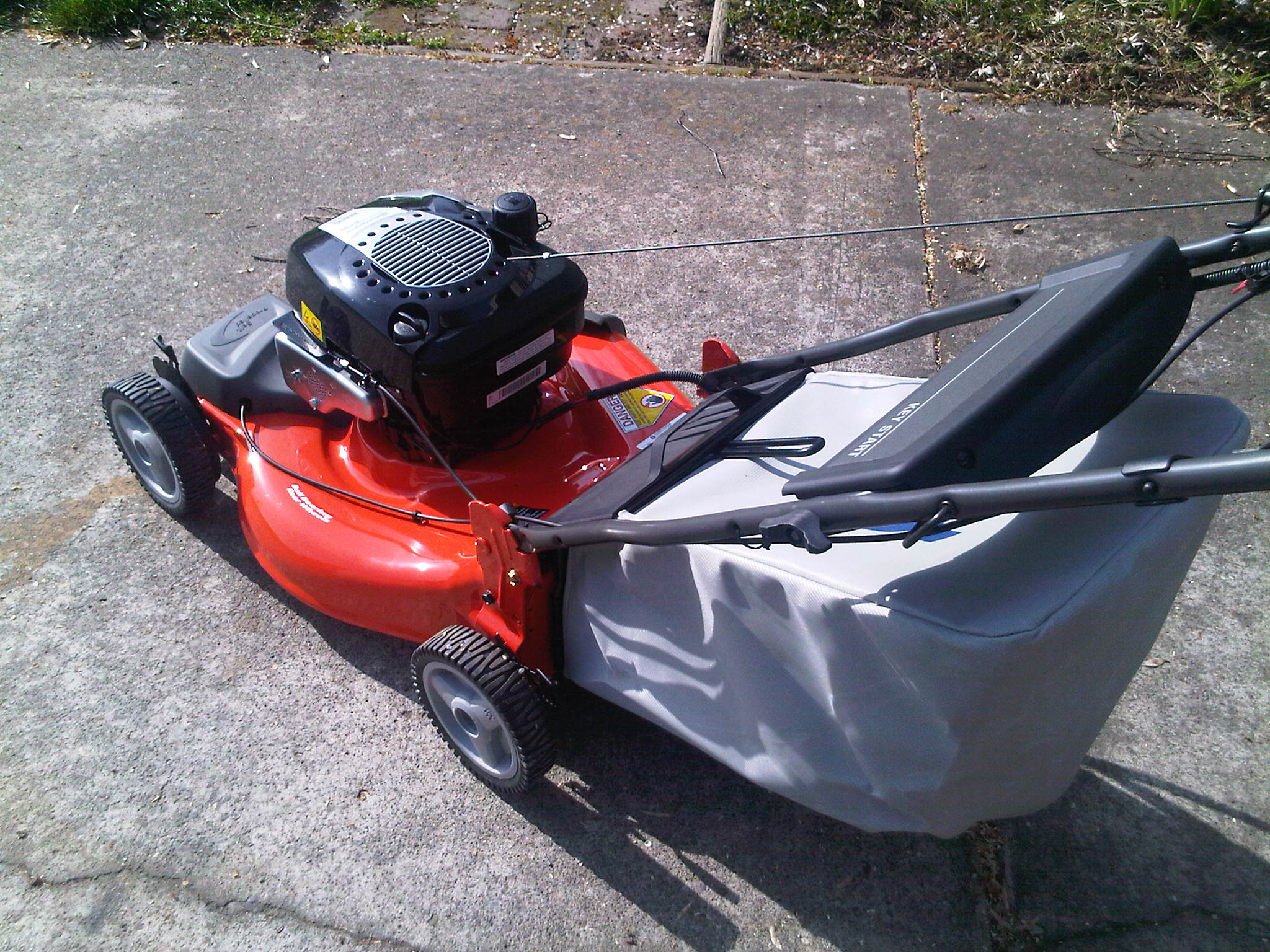 the red lawn mower is parked on the sidewalk