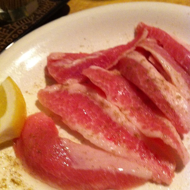 a white plate topped with sliced meat next to lemon wedges