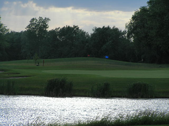 a golf field with water, trees and grass