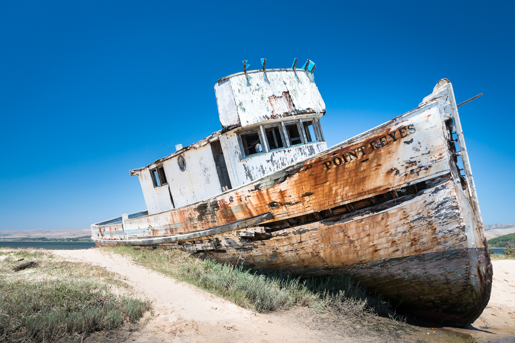 a run down rusted wooden boat sits on top of a dirt path
