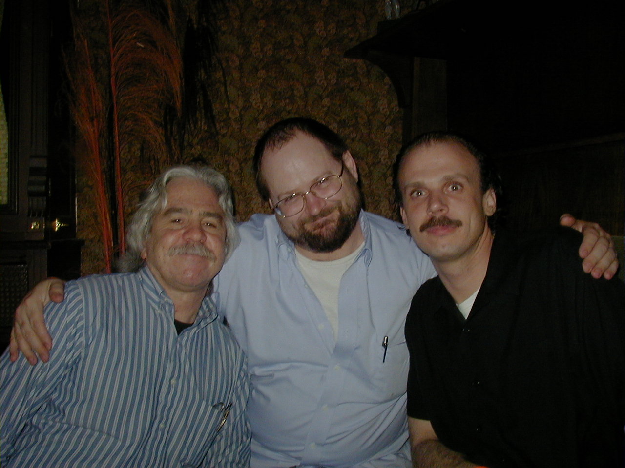 three men sitting next to each other with a man looking at the camera