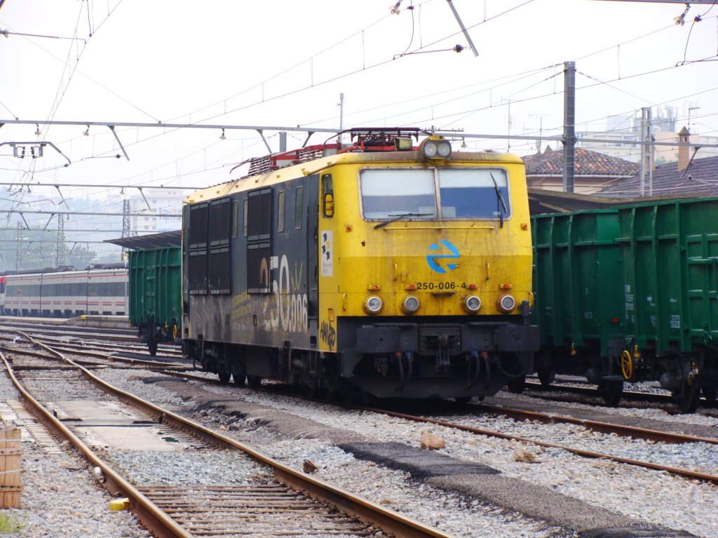 a yellow train is parked on the tracks by some green containers
