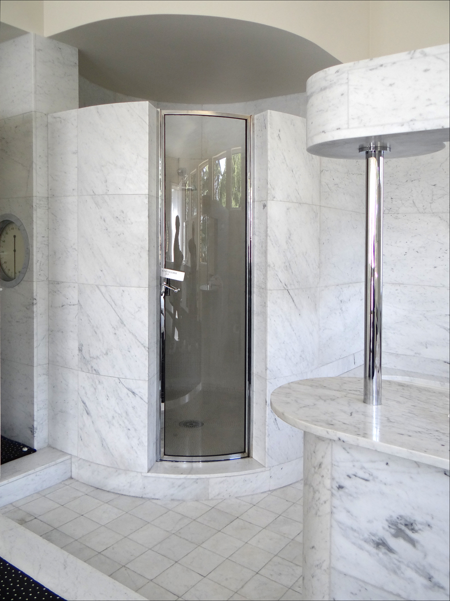 the room is made of marble and features a curved corner shower