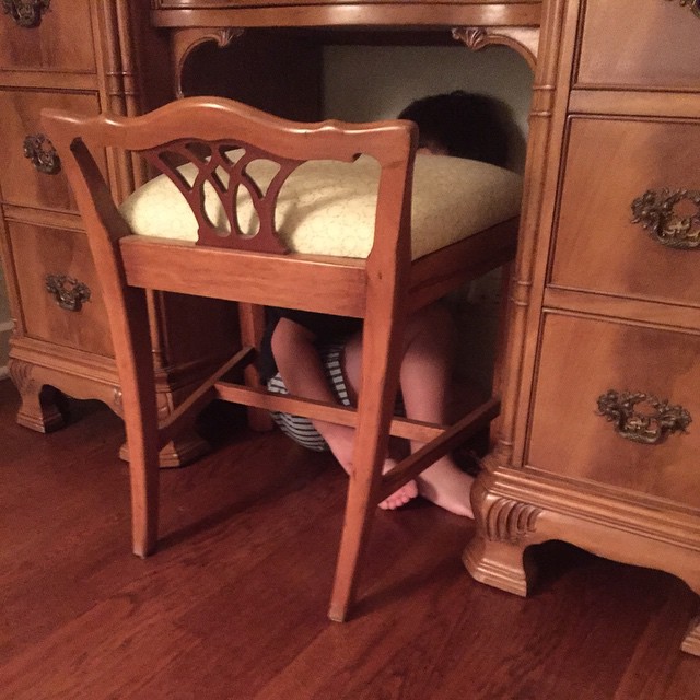 a young child under a chair next to an oak desk