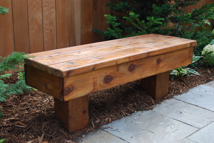 an empty wooden bench sitting outside by some bushes