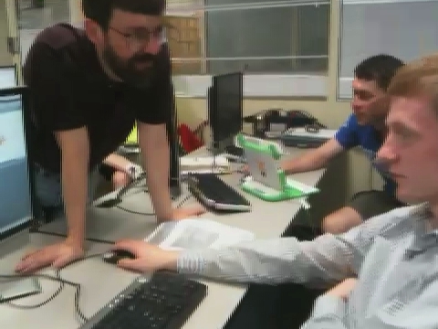 several men sitting around a computer working on the same computer