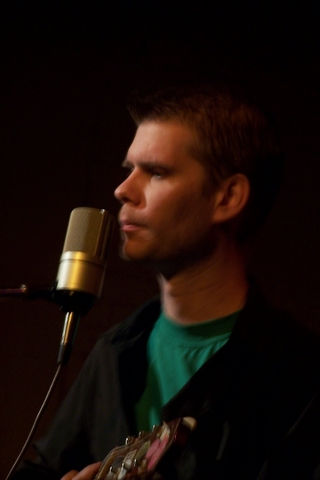 a man in green shirt playing guitar and a microphone