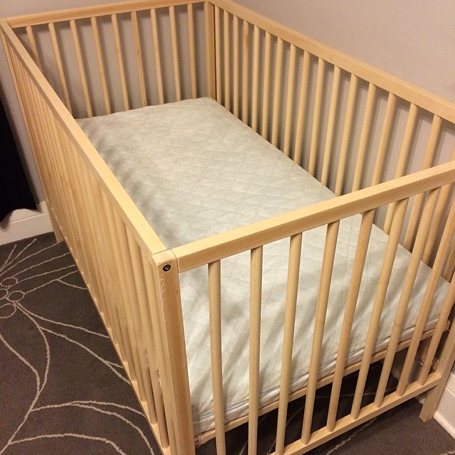 a small wooden crib with white covers and pillow