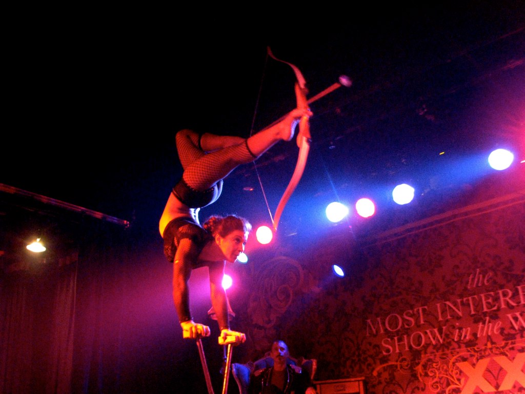 a woman standing on top of a pole performing with arrows