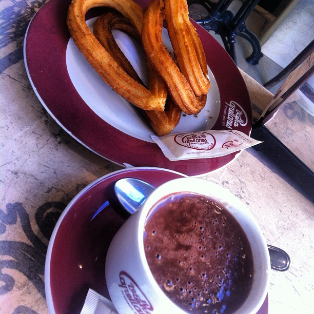 two churros on the plate next to a cup of chocolate drink
