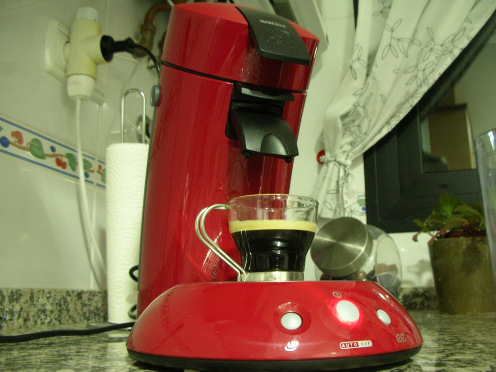a red coffee maker with a glass of espresso in it