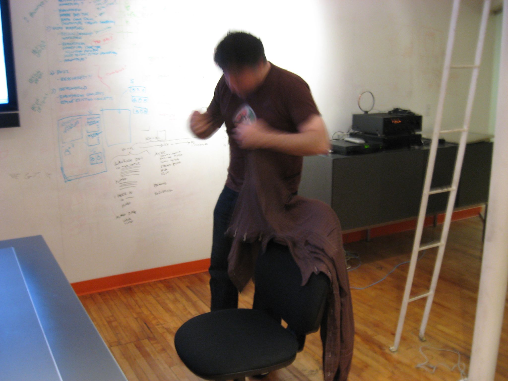 a guy standing on top of a chair near a whiteboard