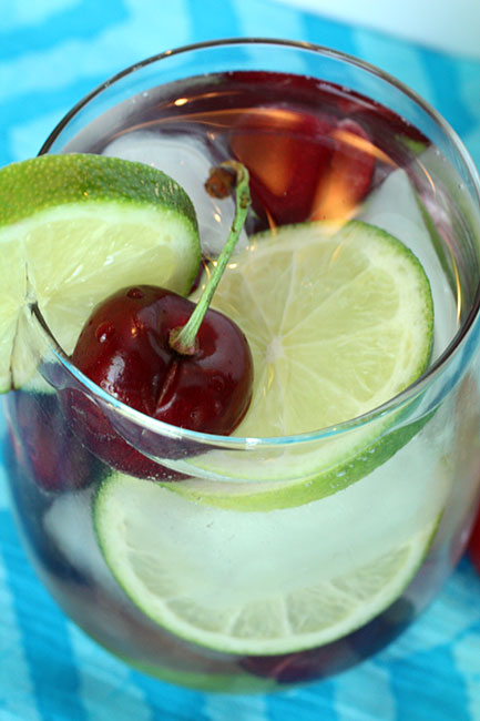 a red cherry and lime drink in a glass on a table cloth