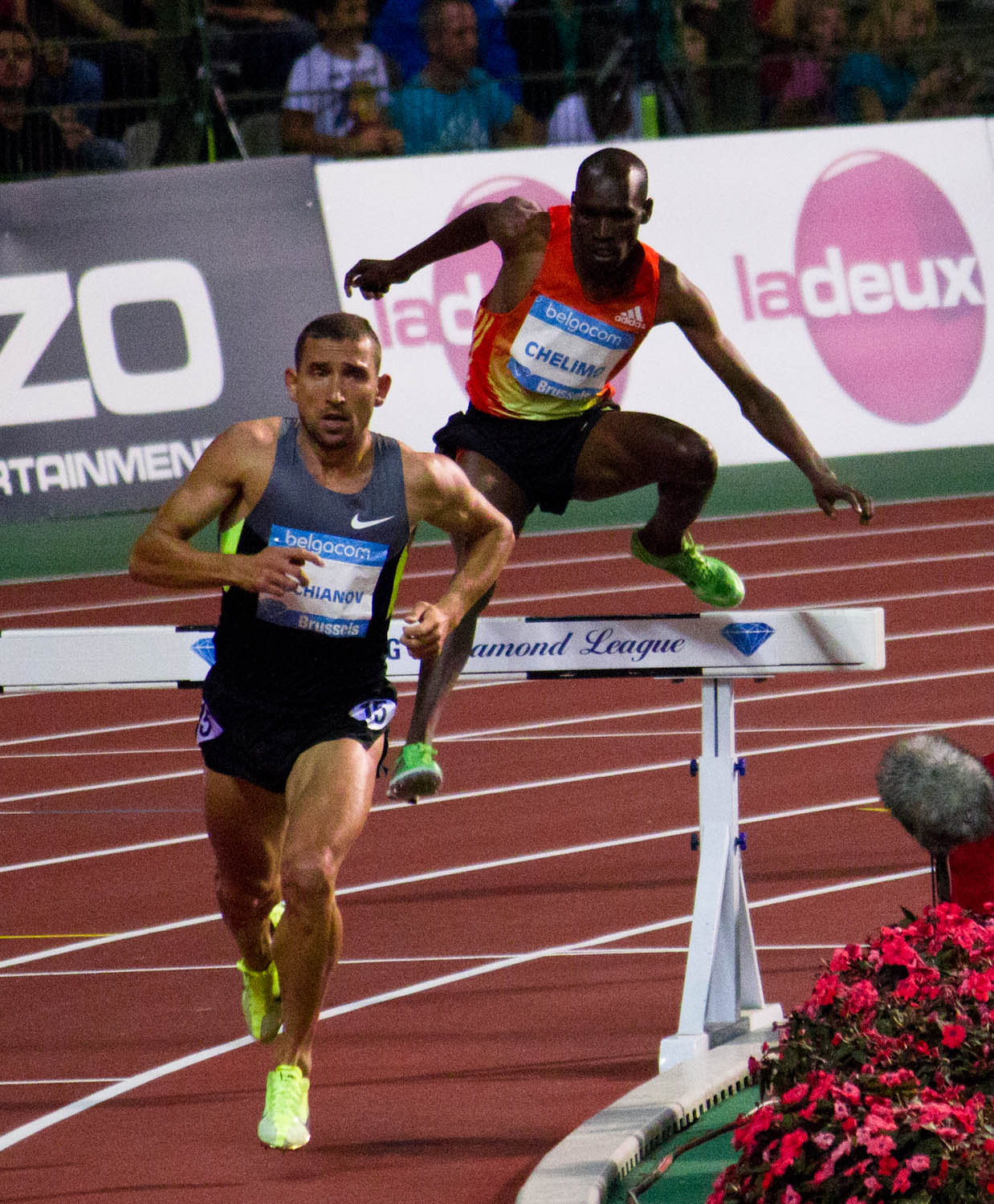 two men are running in a race, one has his leg up as the other looks towards