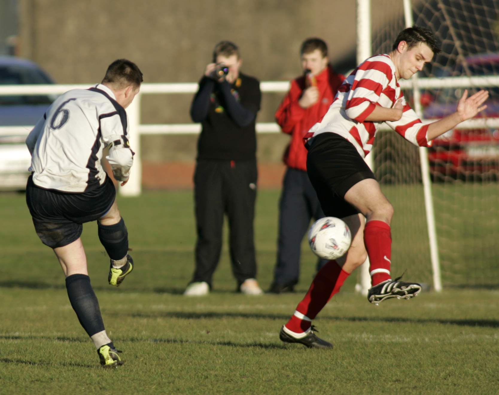 two soccer players kicking a soccer ball toward a goal