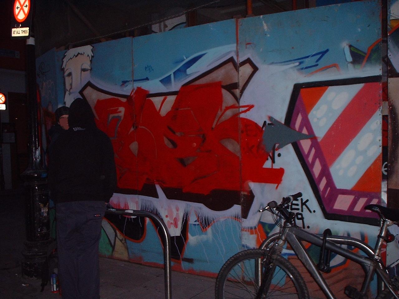 graffiti on the side of the wall depicts two men, one looking at a bike