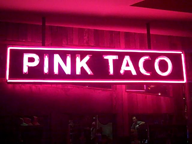the pink taco neon sign is against a wall