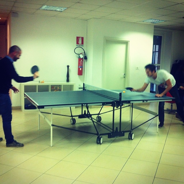 two men playing table tennis indoors in a small room
