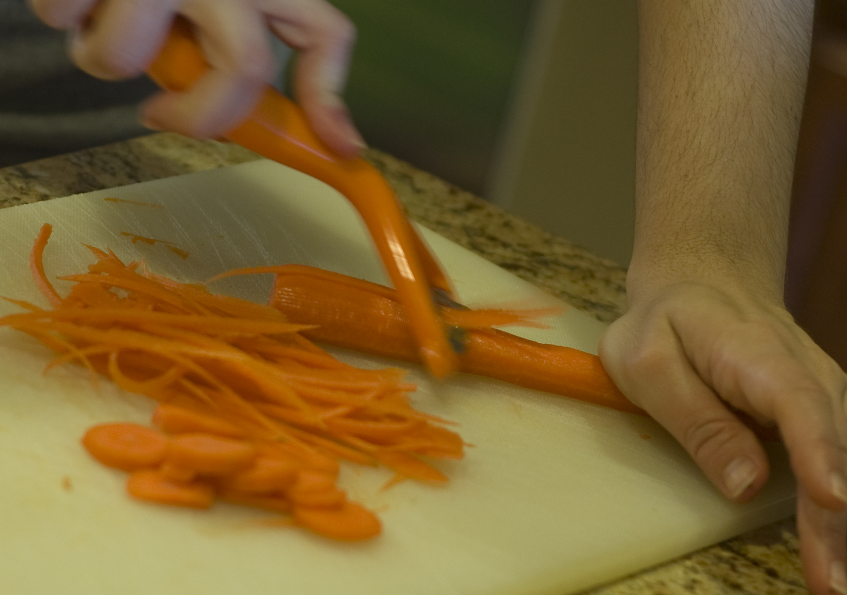 two hands holding orange utensils slicing and serving carrots