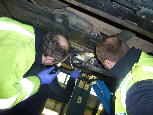 two men working under a vehicle with one using a drill