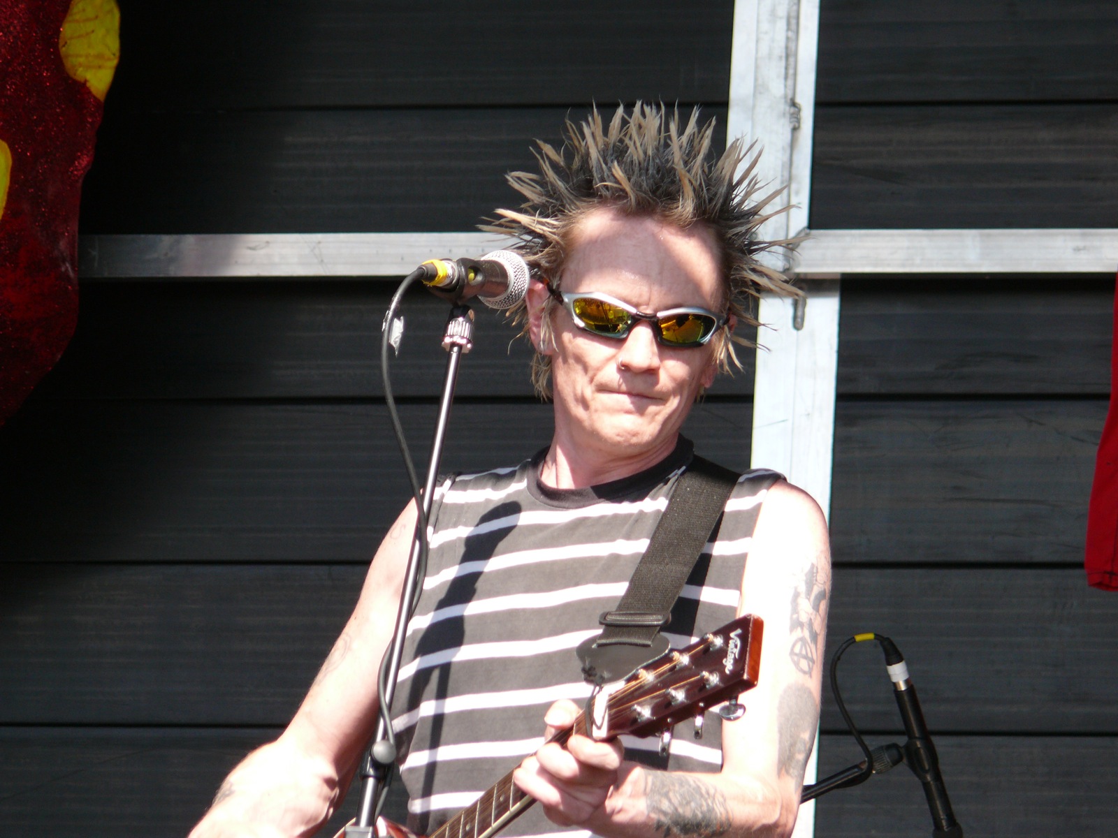 a man with spike hair plays guitar in front of a microphone