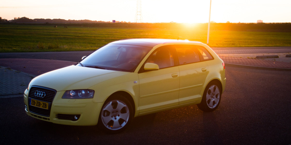 an yellow car parked at sunset with the sun in the background