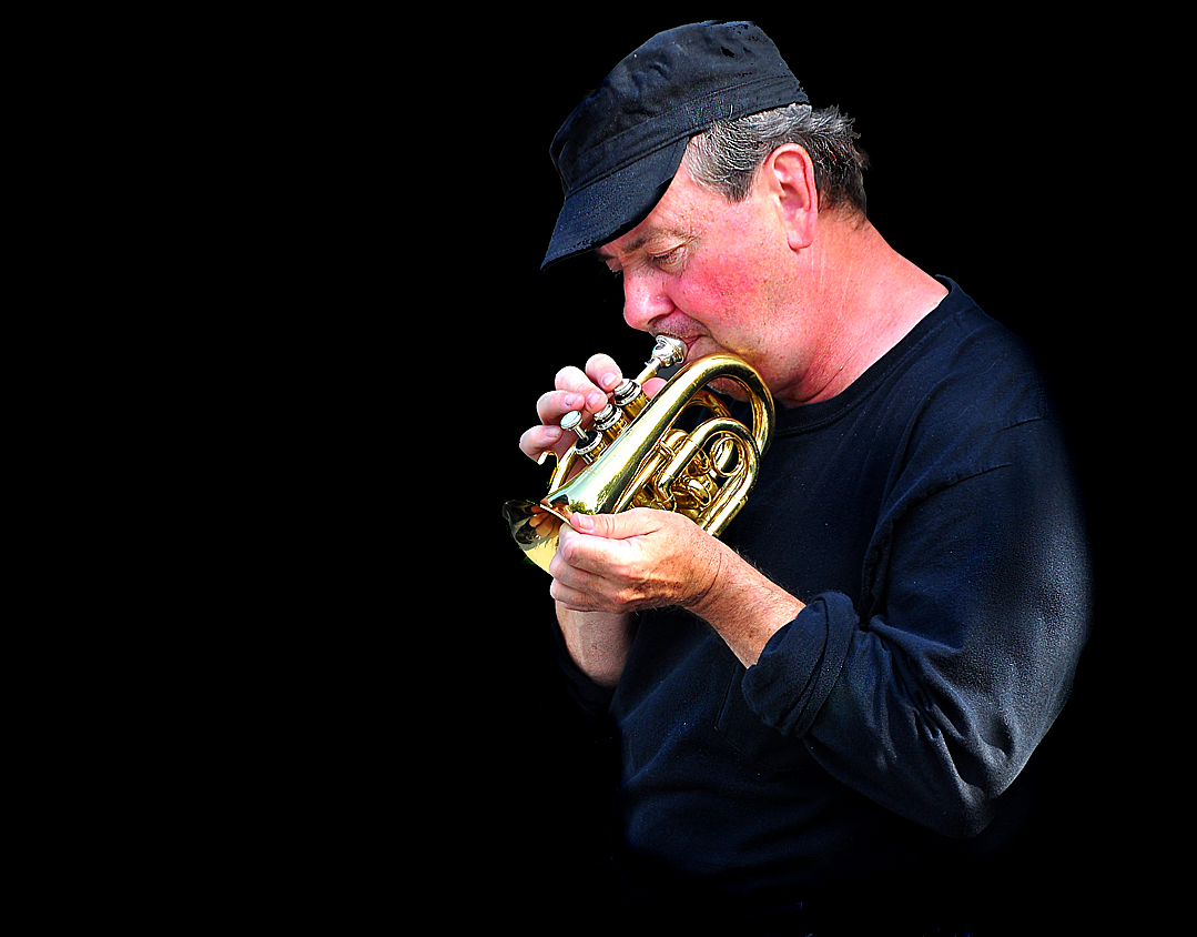 man playing trumpet with dark background in studio