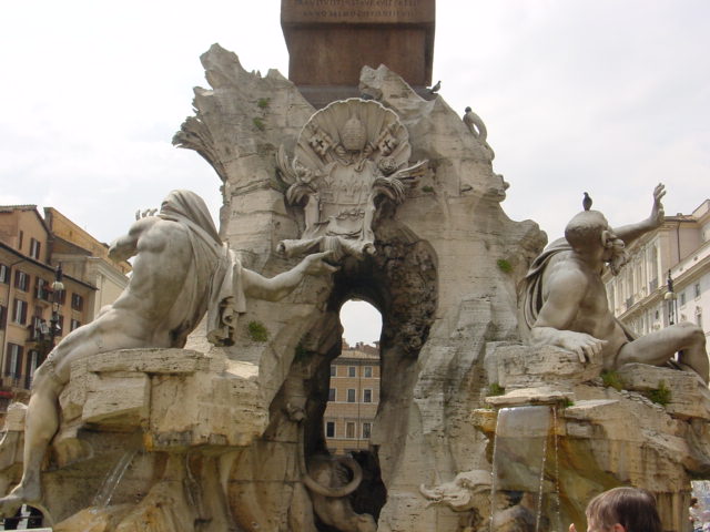 a stone fountain with statues around it with a clock tower in the background