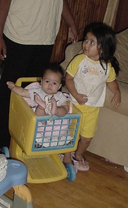 two small children sitting in a walker by a baby cake