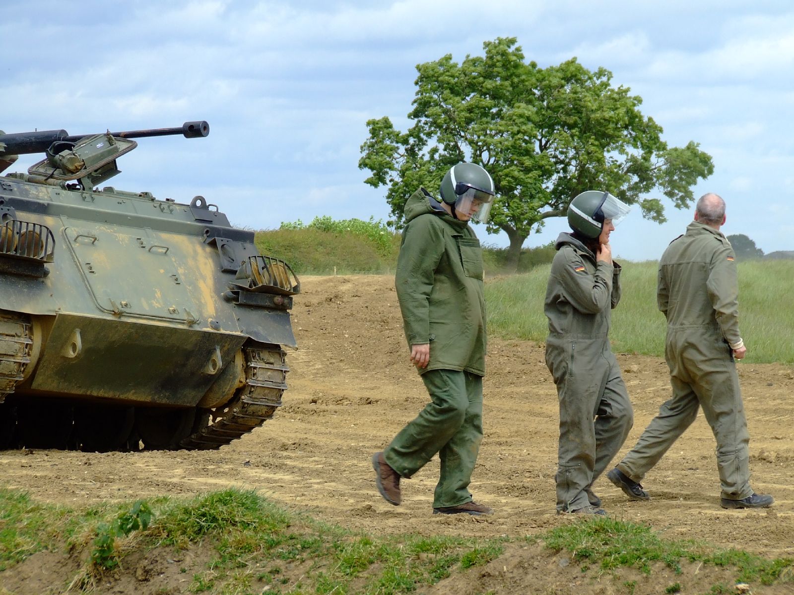 three soldiers walk past a military tank