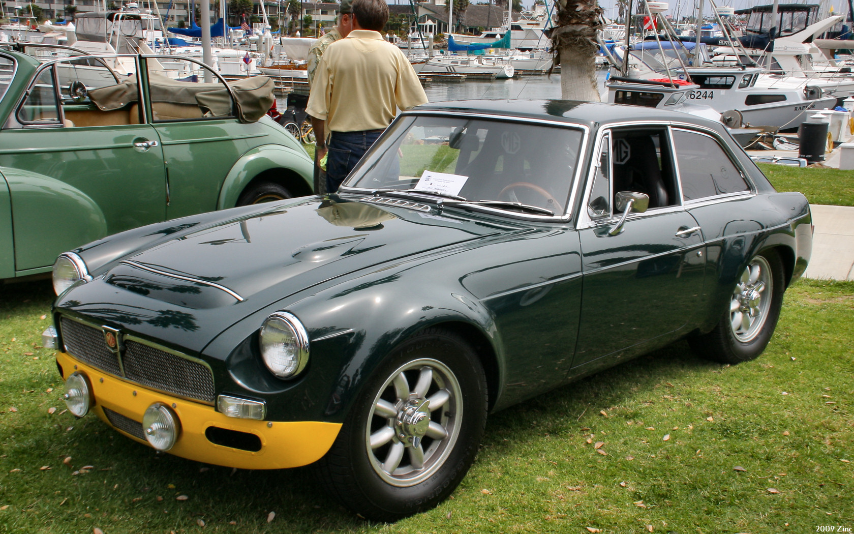 people stand near an old green and yellow car