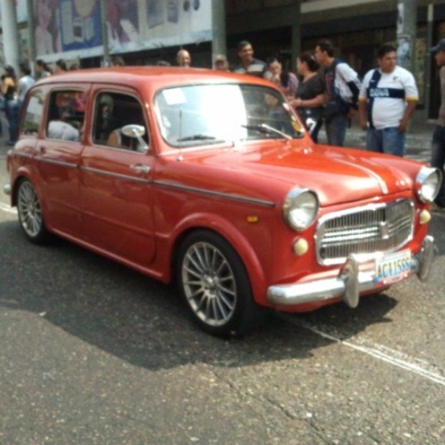 an old red car in the middle of a crowd