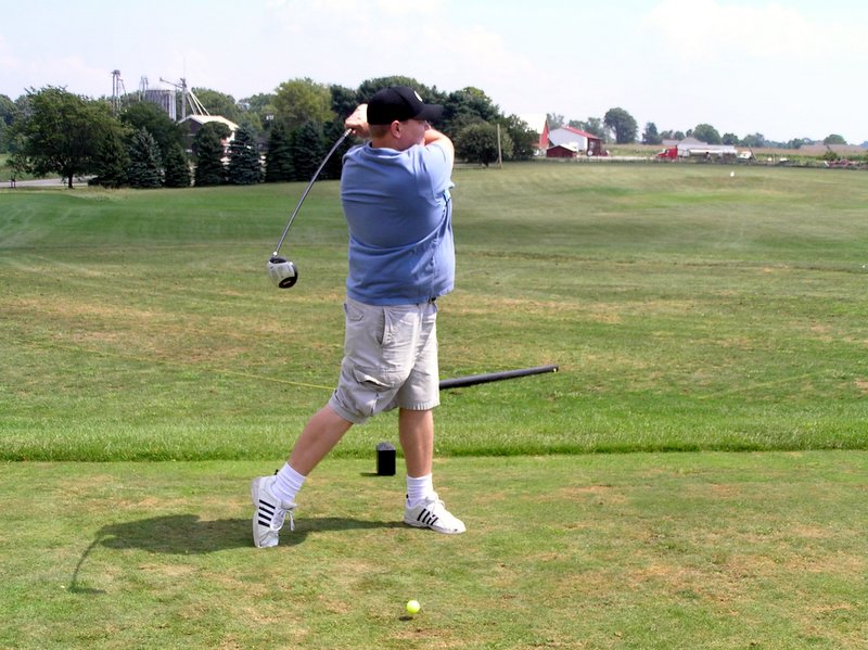 man in blue shirt taking swing at golf ball