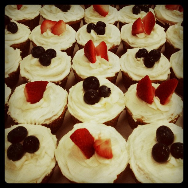 white cupcakes decorated with strawberries and blackberries, sit on a cardboard tray