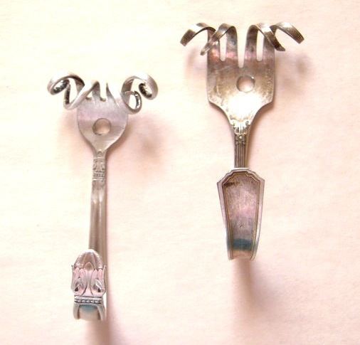 two silver spoons sitting next to each other on a white surface