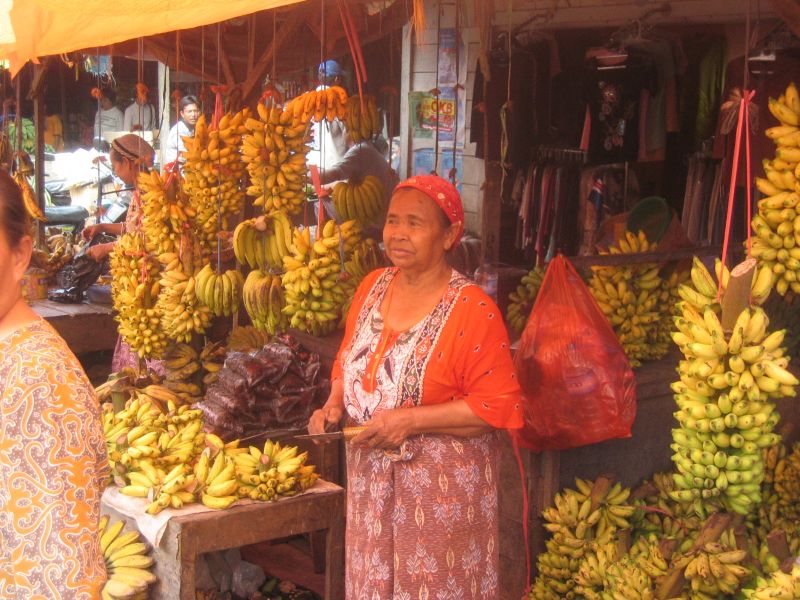 two women at a fruit stand with bunches of bananas