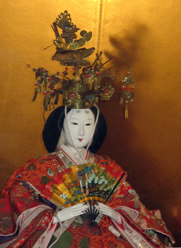 a geisha doll wearing a green and gold helmet