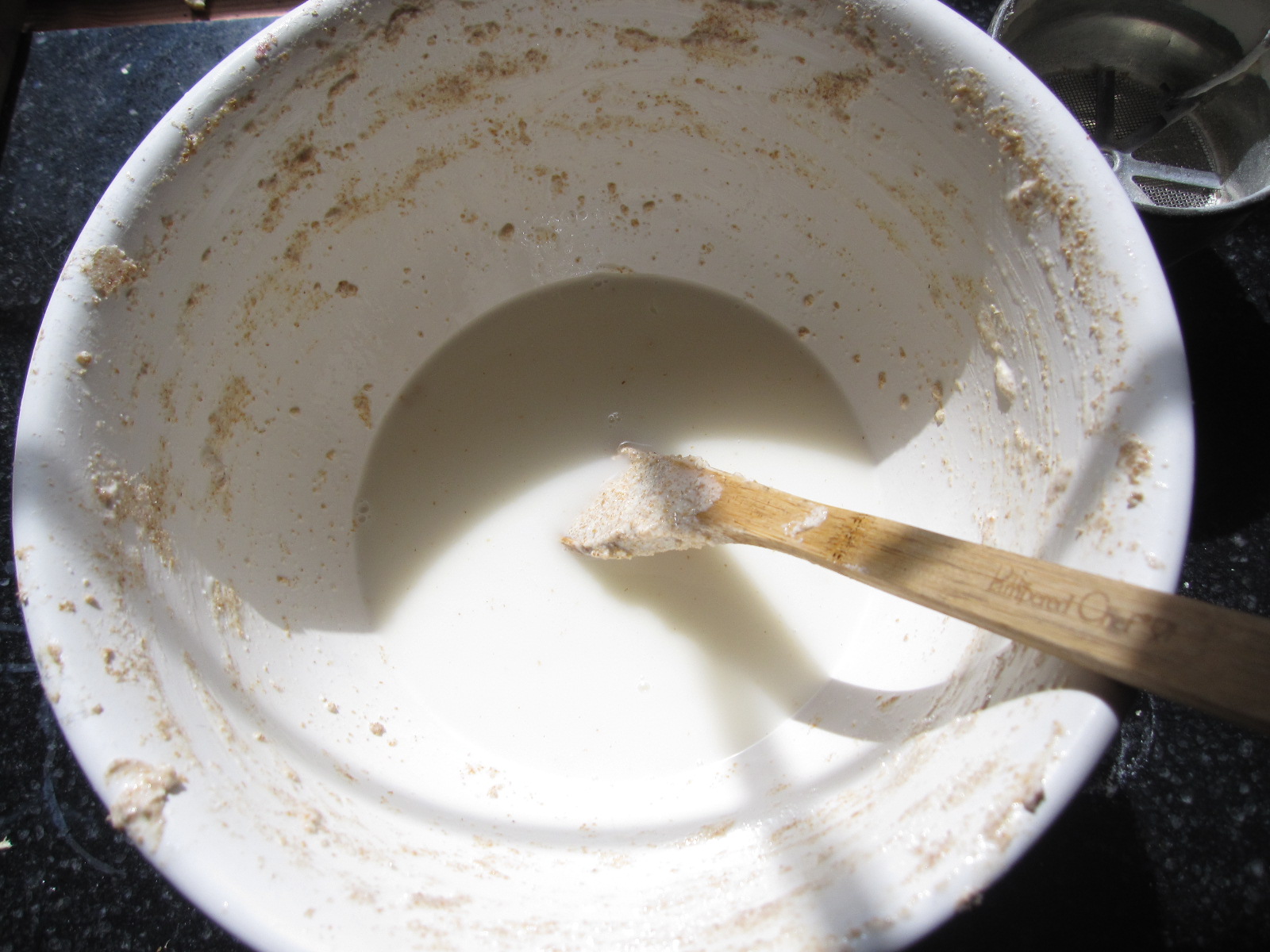 a white bowl with dirty brown paint and a wooden spoon