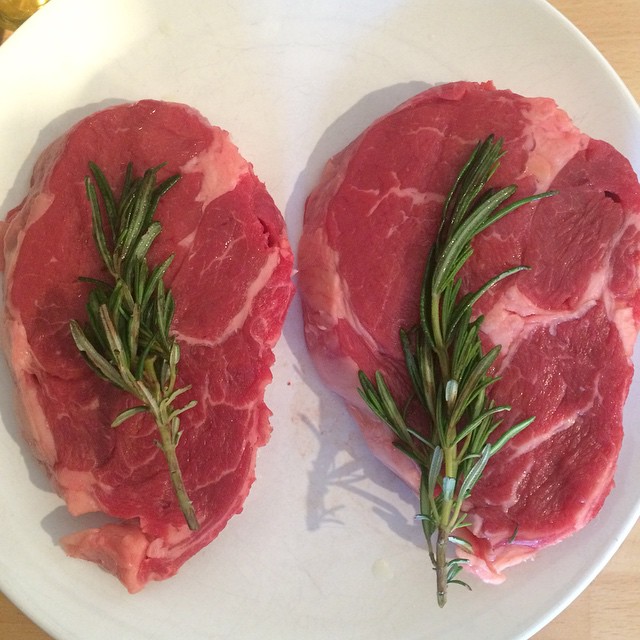 two steaks with rosemary are on a white plate