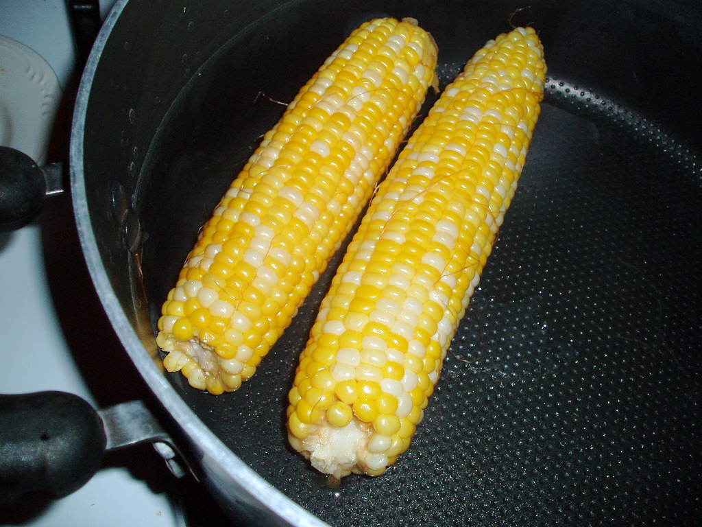 two corn cobs are cooking in a frying pan