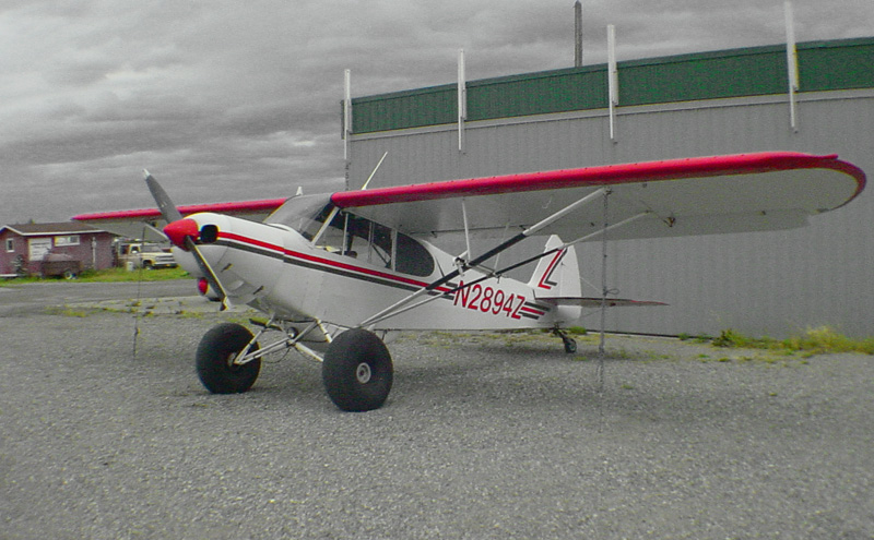 a small red and white plane sitting in the middle of a gravel lot