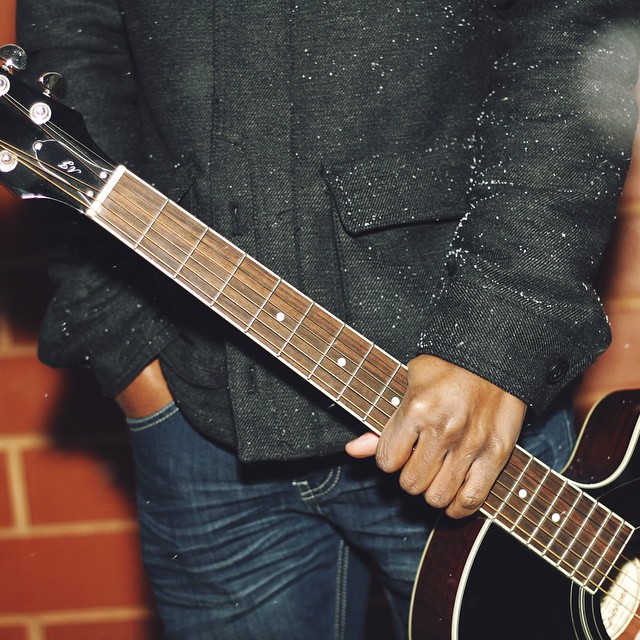 a man in a black jacket holds onto a brown guitar
